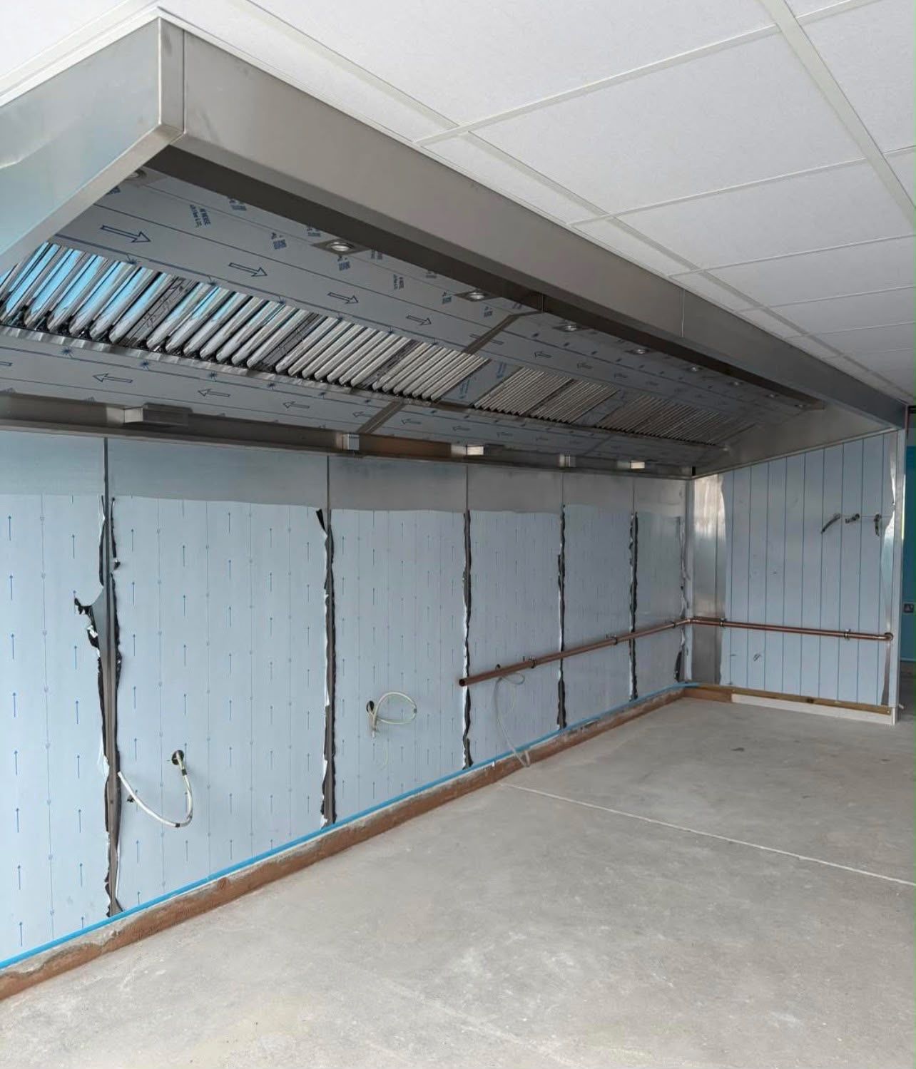 Extraction canopy and stainless steel wall cladding in a kitchen fit-out before equipment is installed