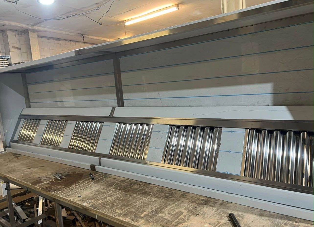 Row of stainless steel baffle grease filters along the face of an installed extraction canopy