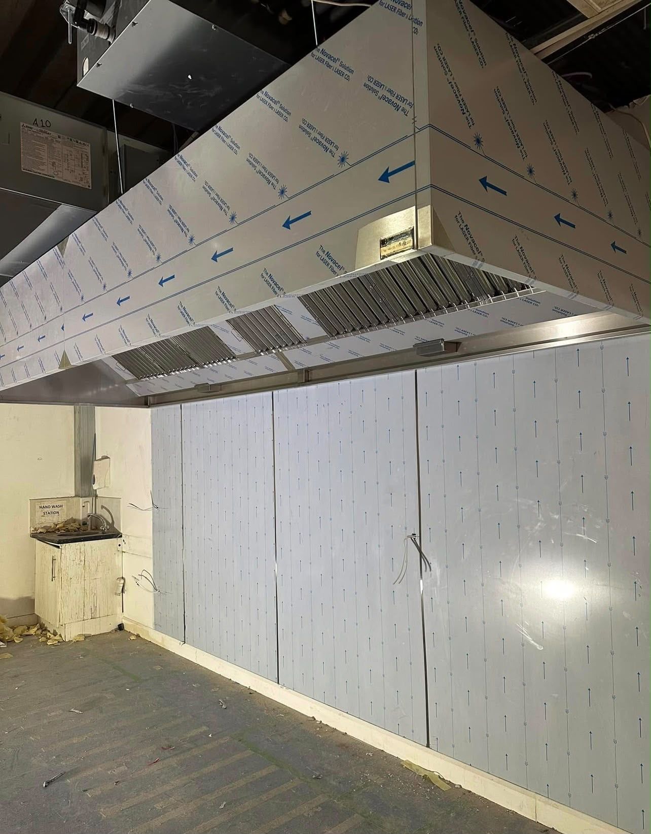 Large stainless steel canopy with ductwork connection above clad kitchen walls