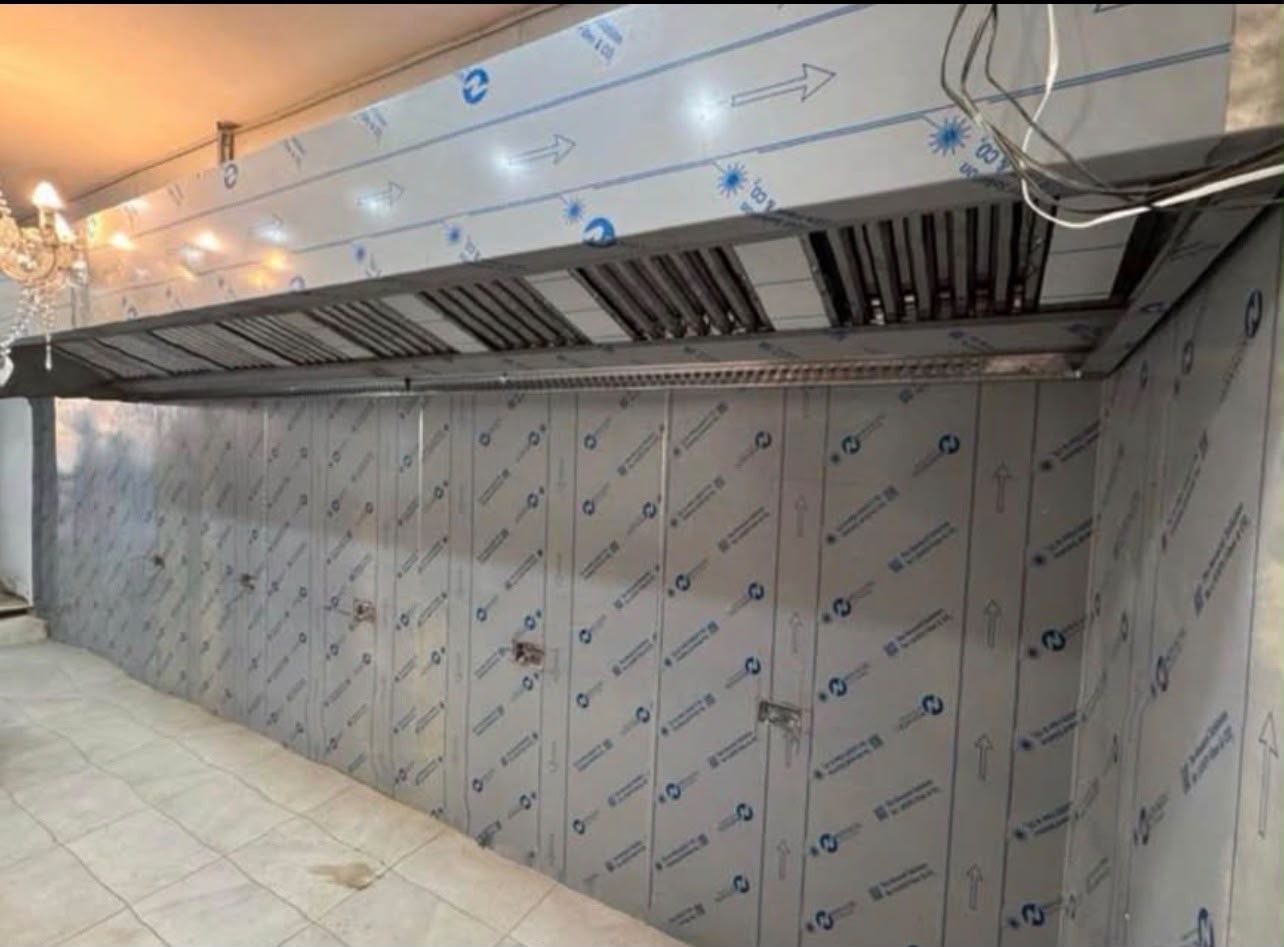 Long wall-mounted extraction canopy above stainless steel wall cladding in a commercial kitchen