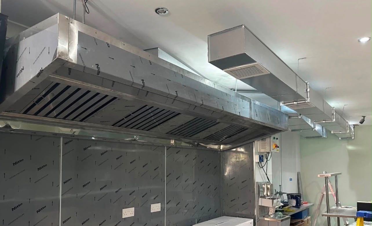 Stainless steel extraction canopy with baffle grease filters over a commercial kitchen cookline