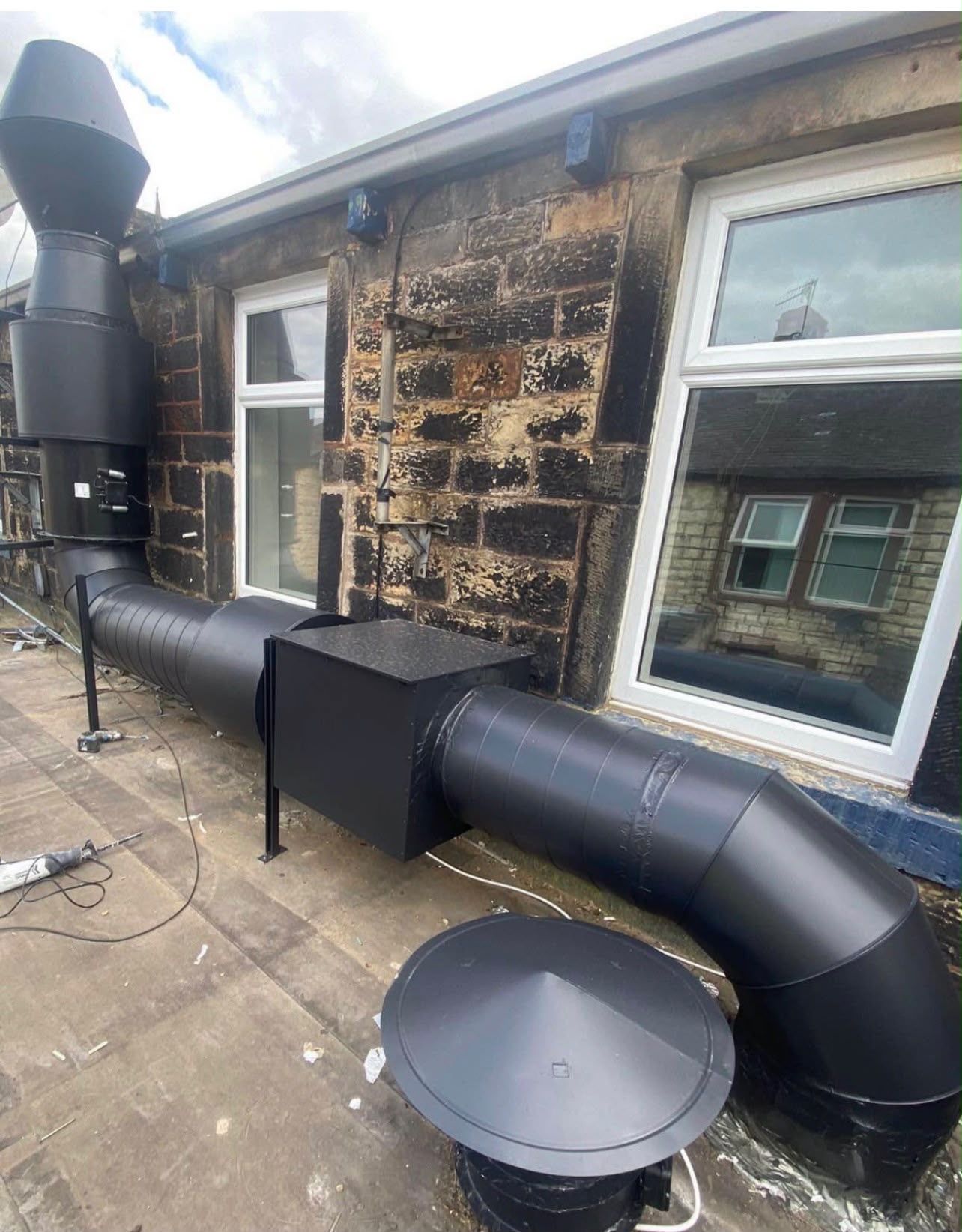 Black-finished extract ductwork and housing across a flat roof beside a discharge cap