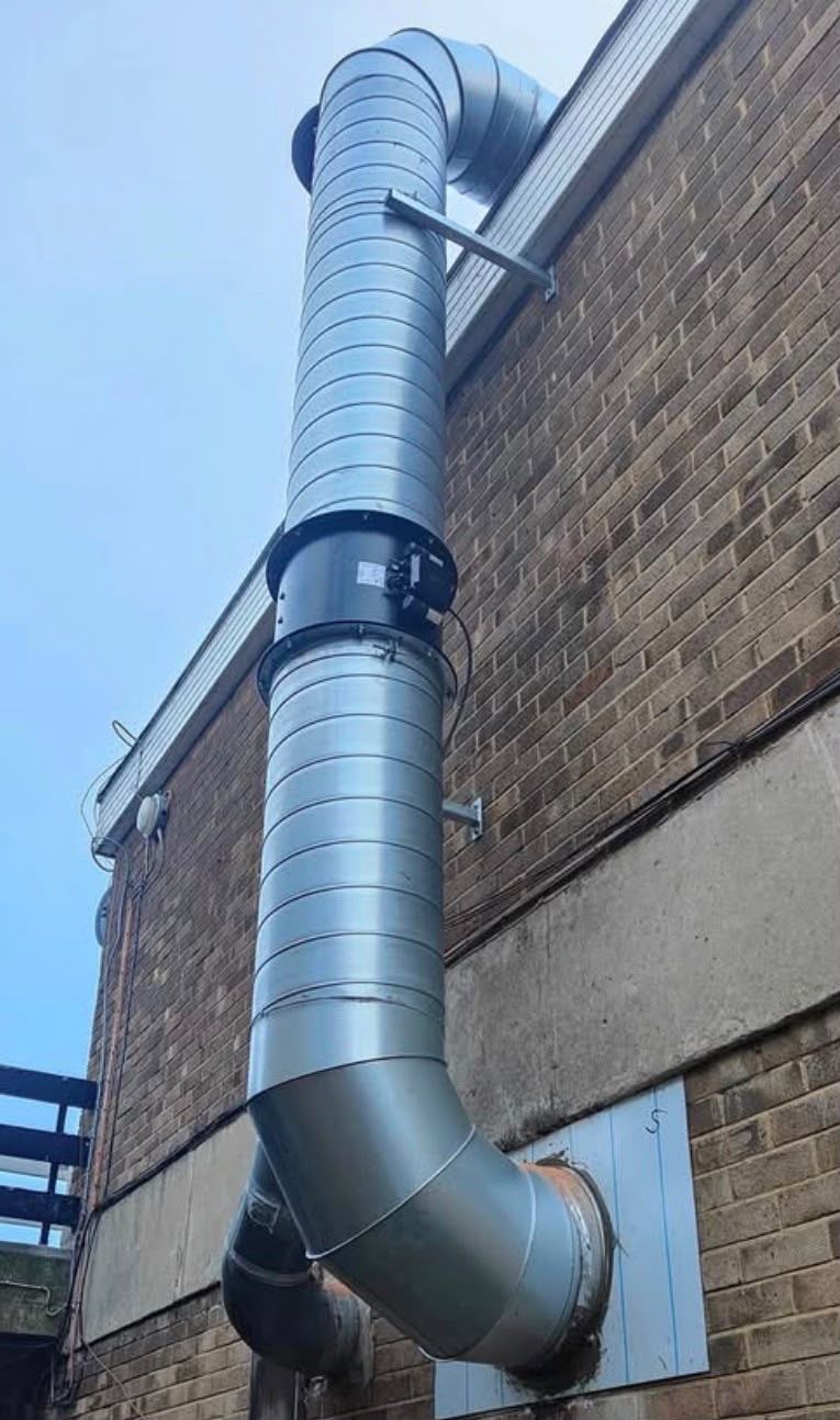 Galvanised spiral ductwork bracketed to a brick elevation with a bend at ground level