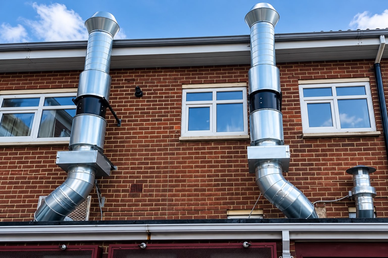 Twin stainless steel extraction ducts with in-line fans and weather cowls on a brick building