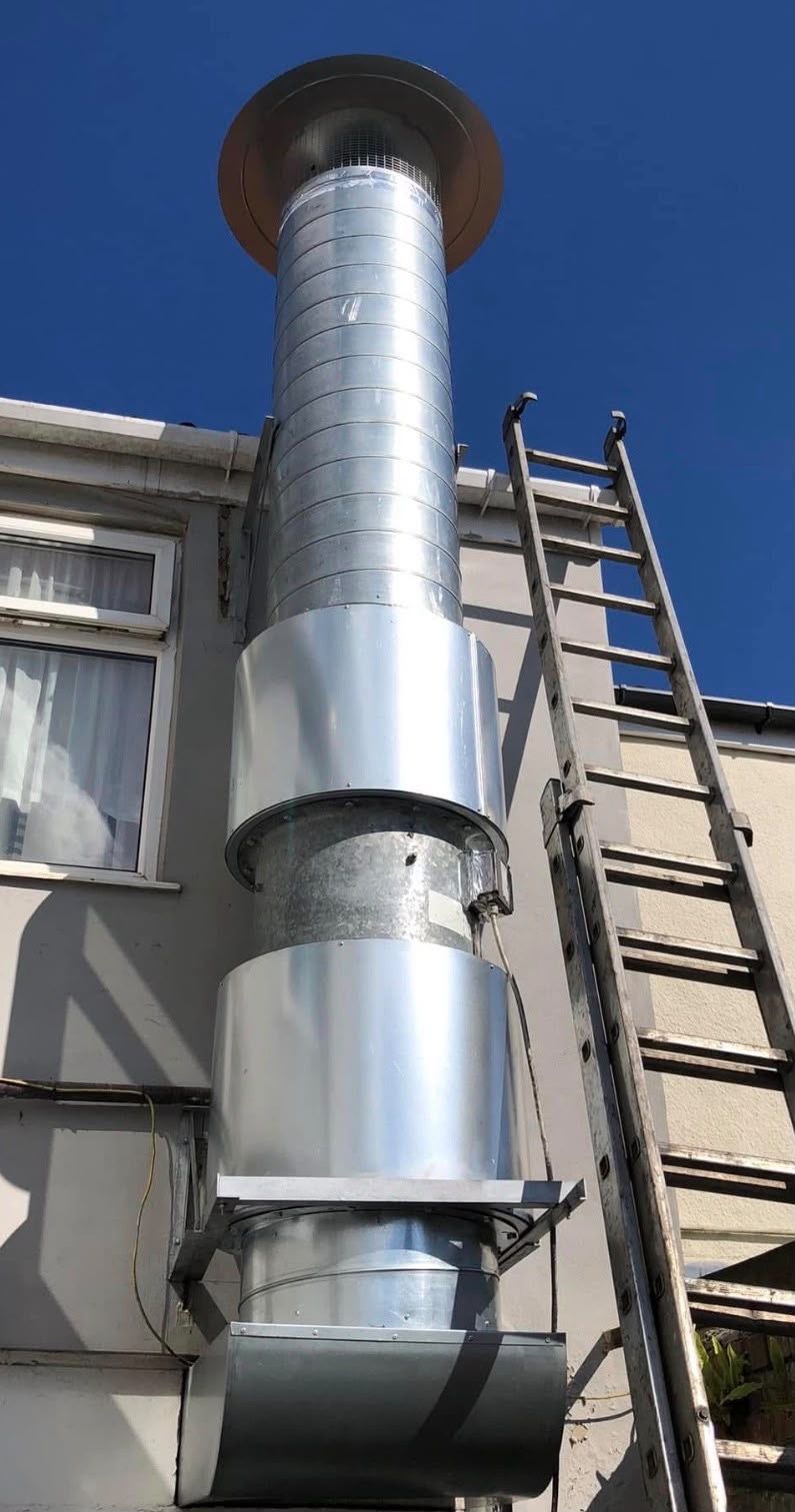 Vertical spiral ductwork rising up an external wall to a discharge cowl, with a ladder beside it