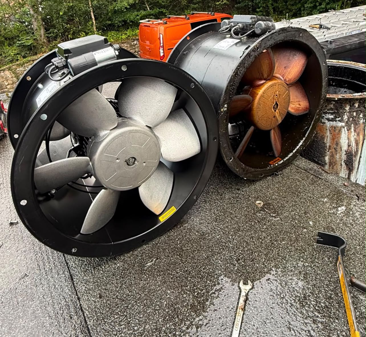 Worn axial extractor fan beside a new replacement fan on a kitchen roof